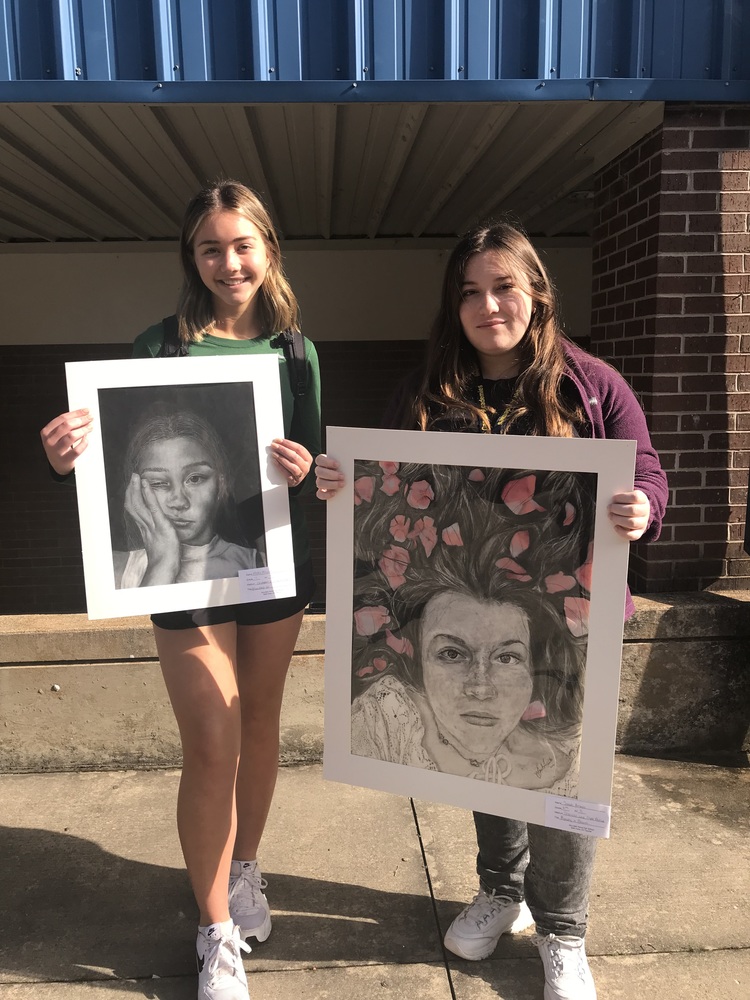 a picture of two teen girls holding charcoal artwork