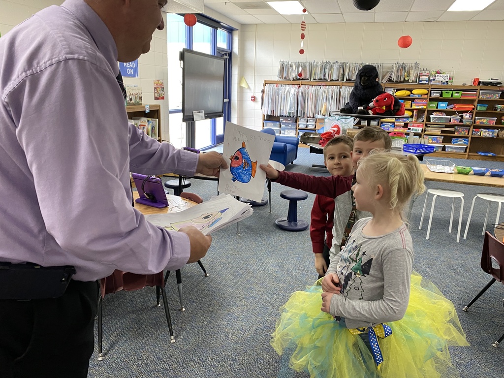 a child handing a principal a colored paper with a fish on it.