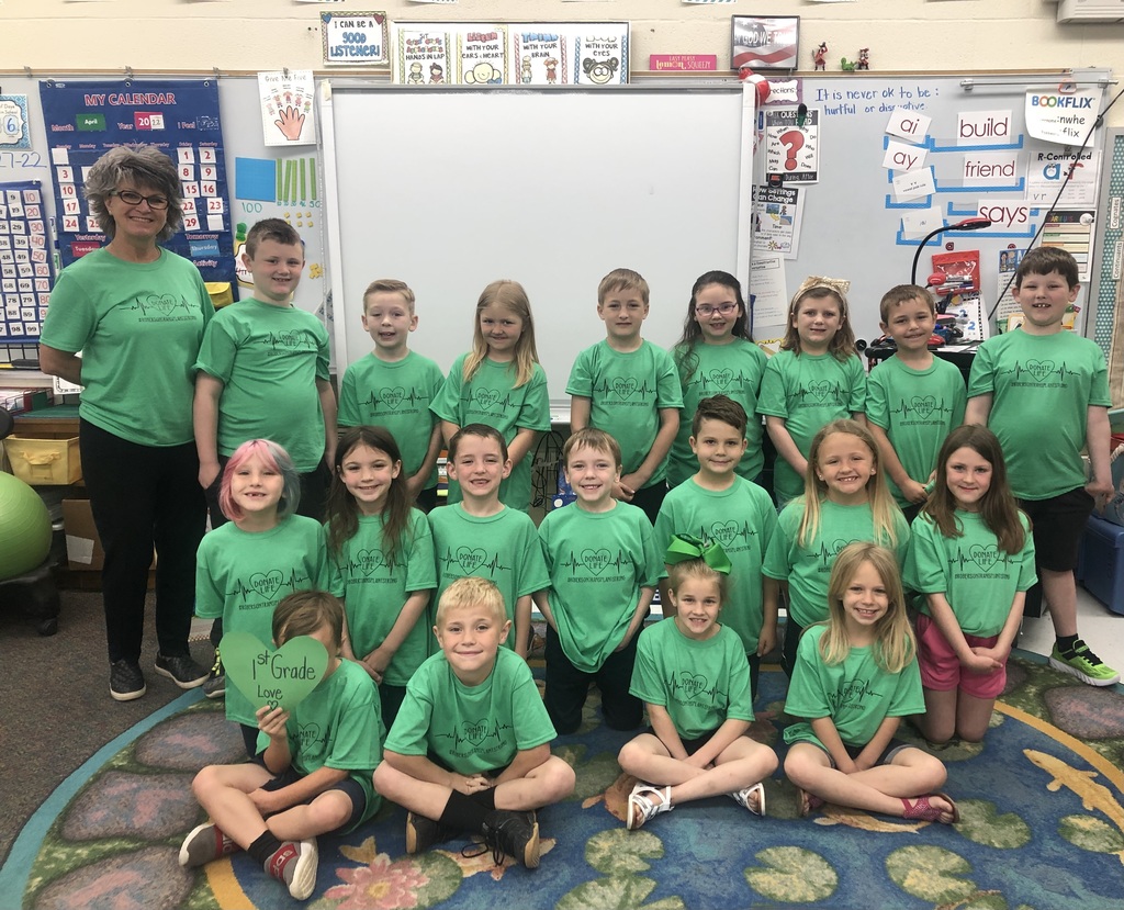 a teacher with a class of first graders in green shirts
